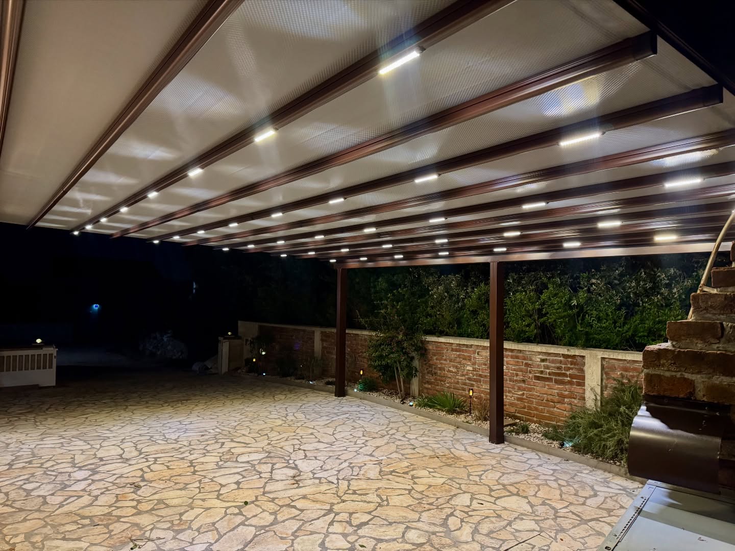 Close-up of integrated LED lighting on pergola awning profile — brown aluminum system, night view, Turkey export